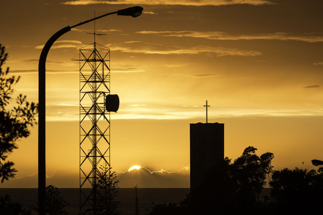 Sunrise Signals - Sunrise over the Pacific Ocean silhouetting a cathedral bell tower's cross and a communcations structure both broadcasting their respective signals. Napier New Zealand
